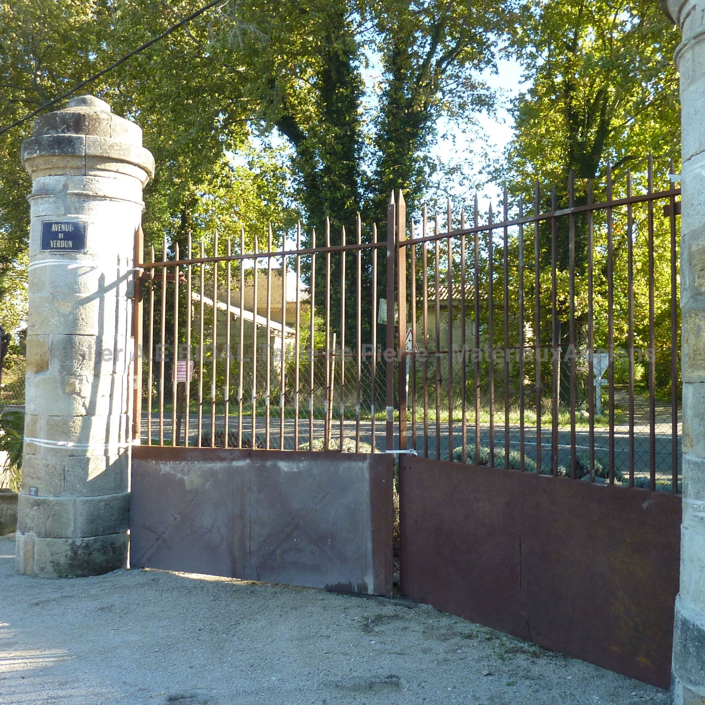 Portail ancien en fer forgé présenté avec un pilier ancien de chaque côté.