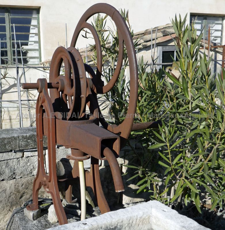 Ancienne pompe manuelle à manivelle sur fontaine en pierre avec double bacs anciens.