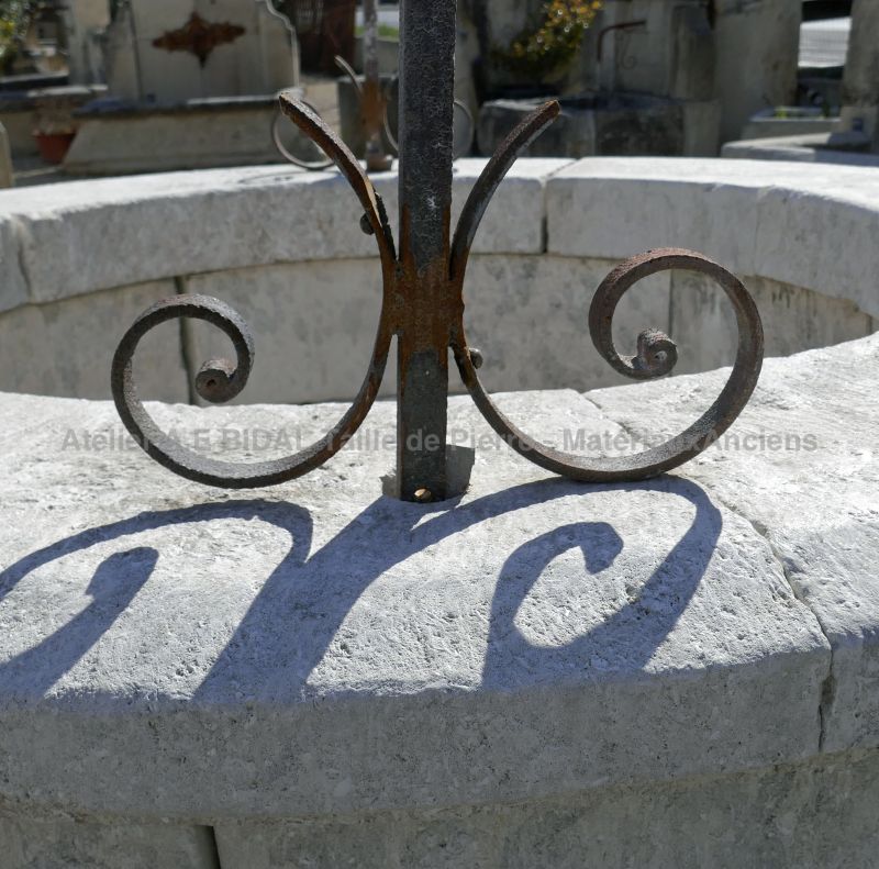 Detail of the stone coping and the wrought iron volute on the stone garden well on sale at Alain BIDAL, Provence.