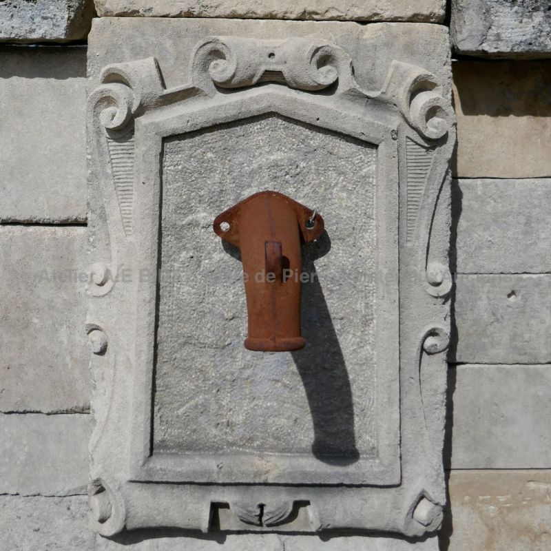 Detail of the metal water outlet and carved stone breastplate on our large stone fountain | Antique fountain for sale in Provence at Bidal Matériaux Anciens.