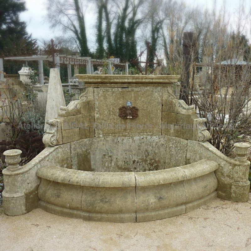 Wall fountain with pediment featuring an ancient iron water spout | Decorative garden fountain in stone.