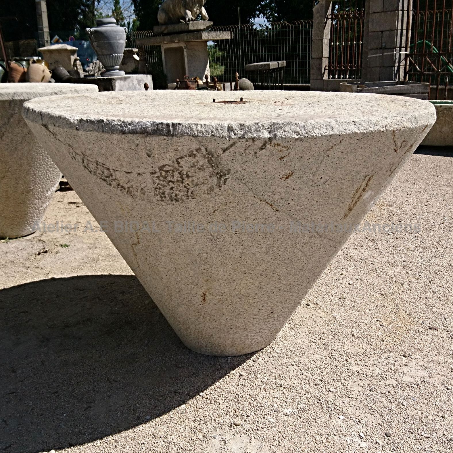 Une table ancienne de forme conique en pierre mono-bloc pour aménager un espce vert.