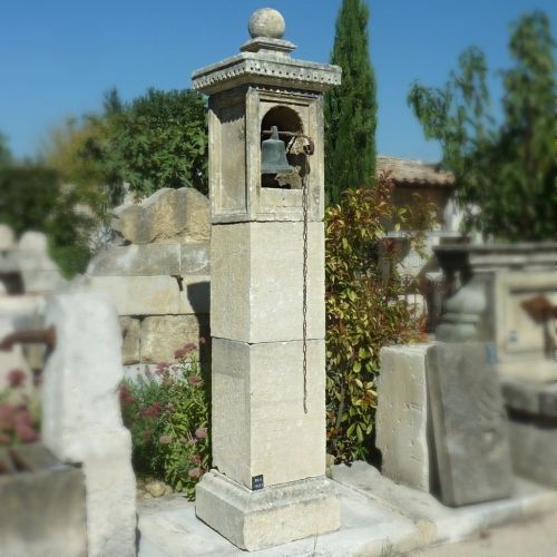 Un élégant pilier d'entrée en pierre naturelle avec niche et cloche ancienne - Alain Bidal en Provence.
