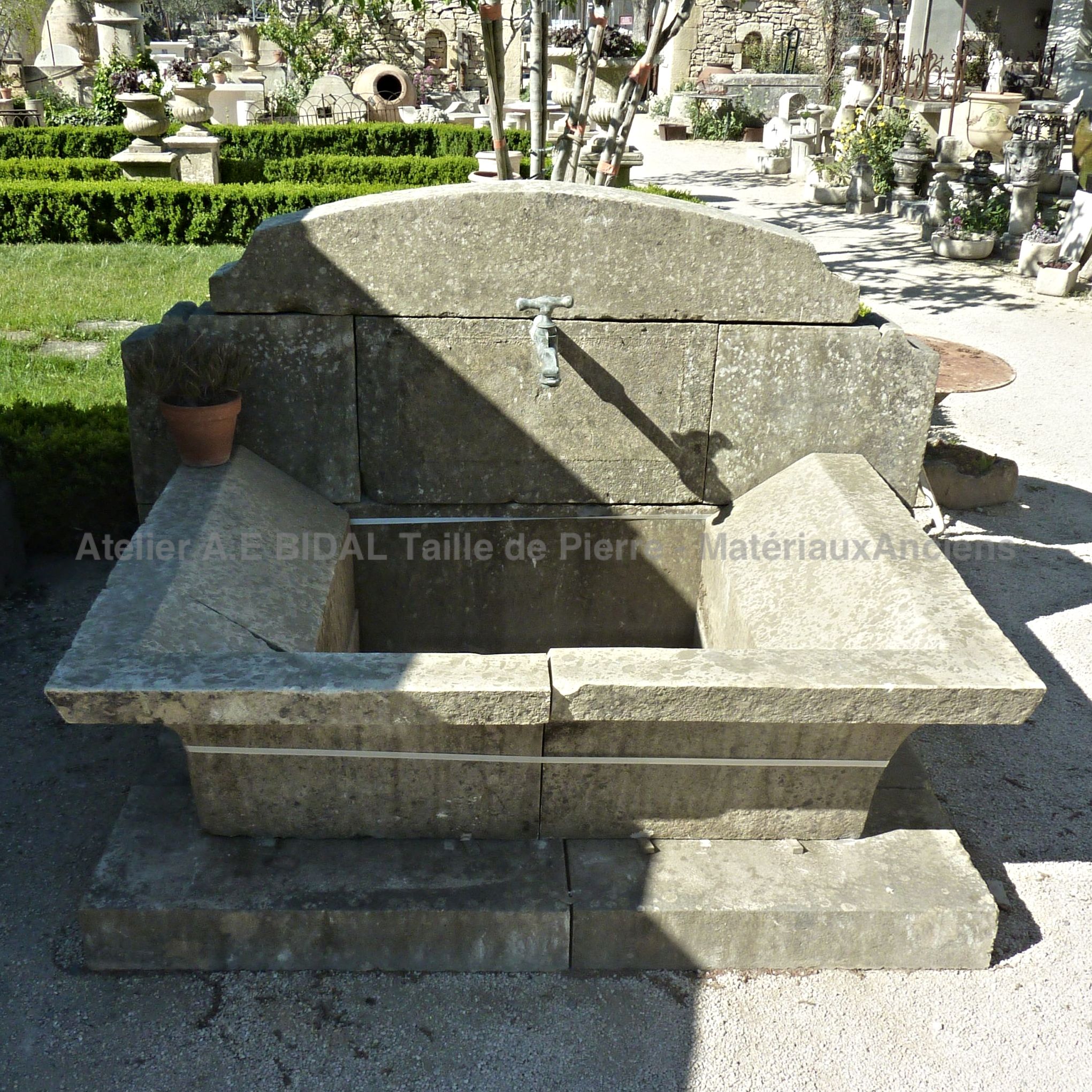 Fontaine murale avec robinet en métal et bassin de style lavoir ancien.