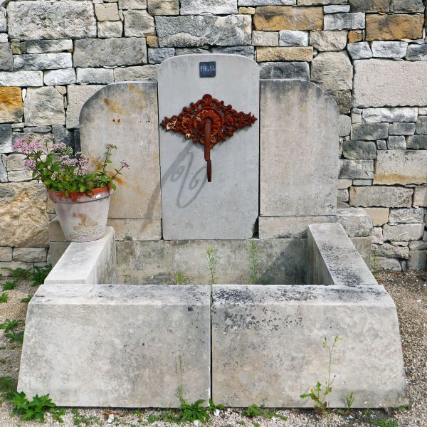 Stone wall fountain with beautiful iron palmette on its pediment.