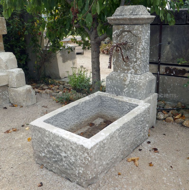 Small garden wall fountain in stone with wrought iron water outlet.