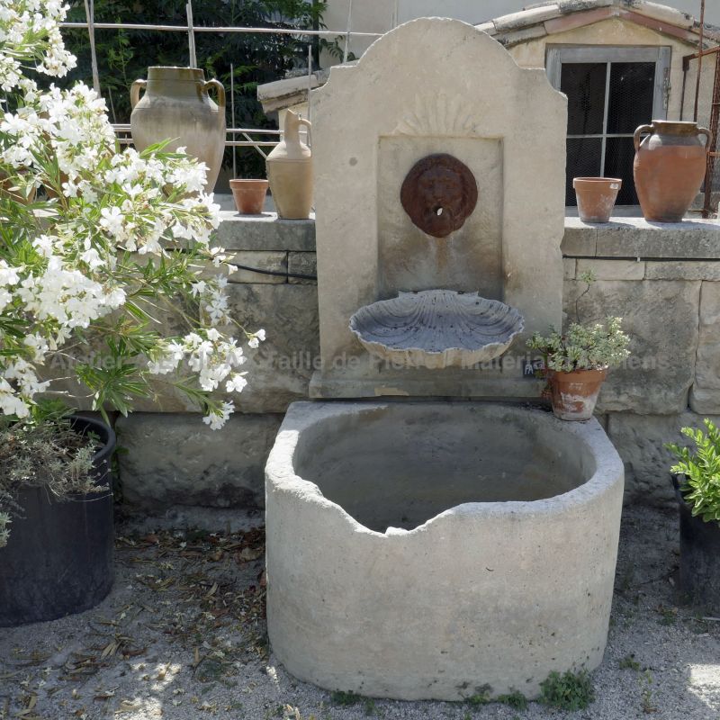 Stone wall fountain with a water outlet representing a lion's head that contrasts with the whitish color of the natural stone.