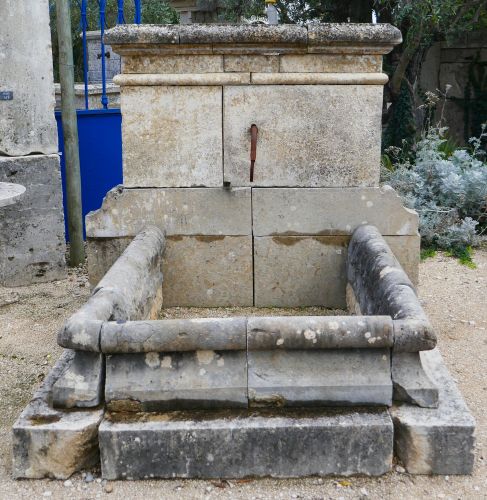 Fontaine ancienne - une fontaine murale en pierre avec détail en fer forgé.