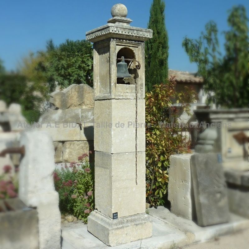 An elegant entrance pillar in natural stone with niche and antique bell - Alain Bidal in Provence.