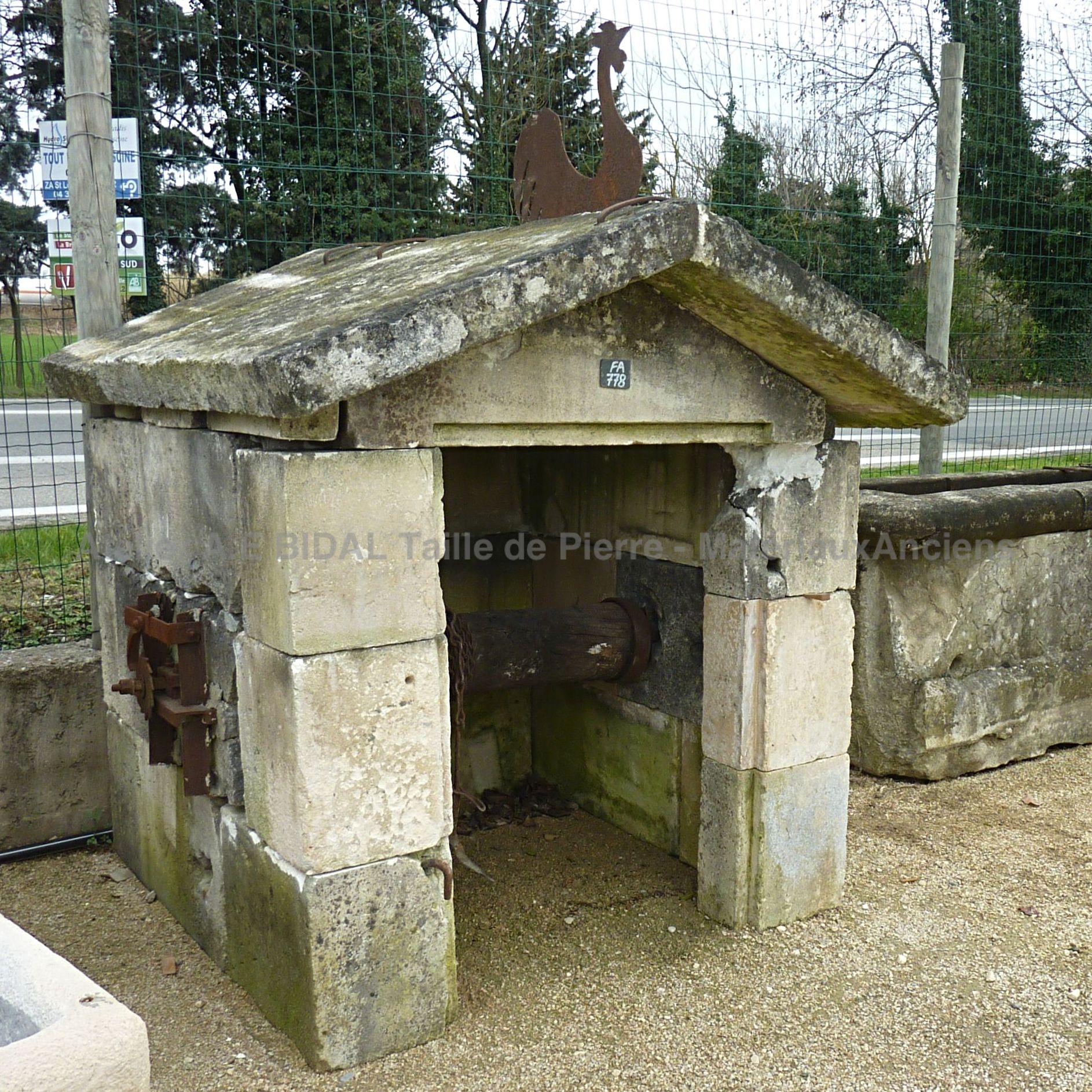 Beau puits en pierre - puits de type maisonnette décoré d'un coq.