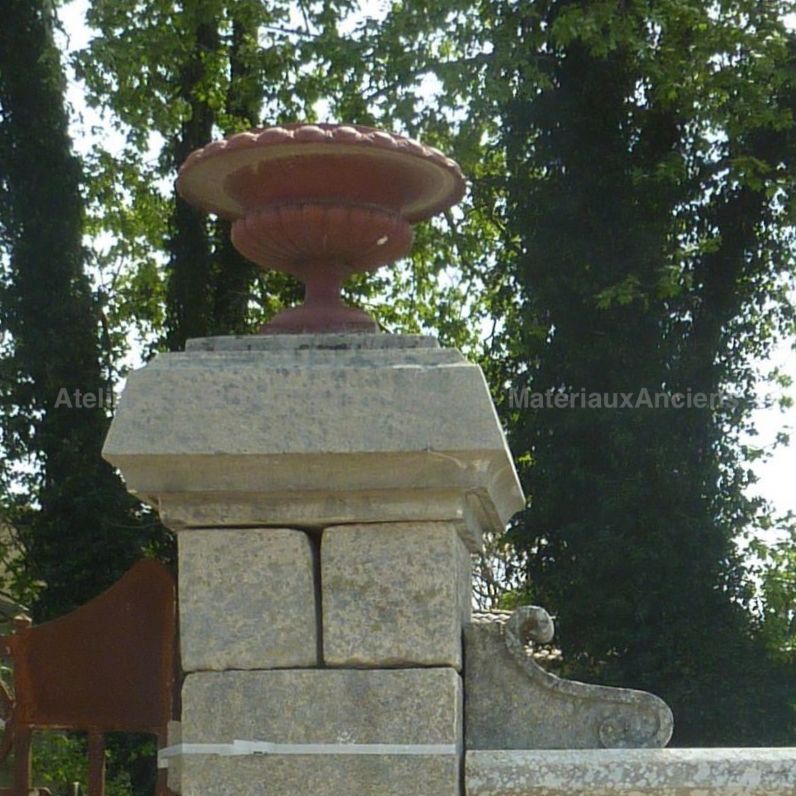 Vase ancien en fonte posé sur le chapiteau d'un pilier ancien en pierre.