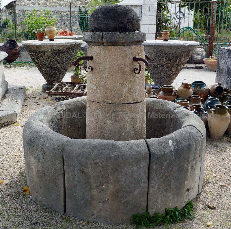 Fontaine centrale en pierre naturelle | Petite fontaine de forme circulaire avec 4 sorties d'eau en fer forgé.