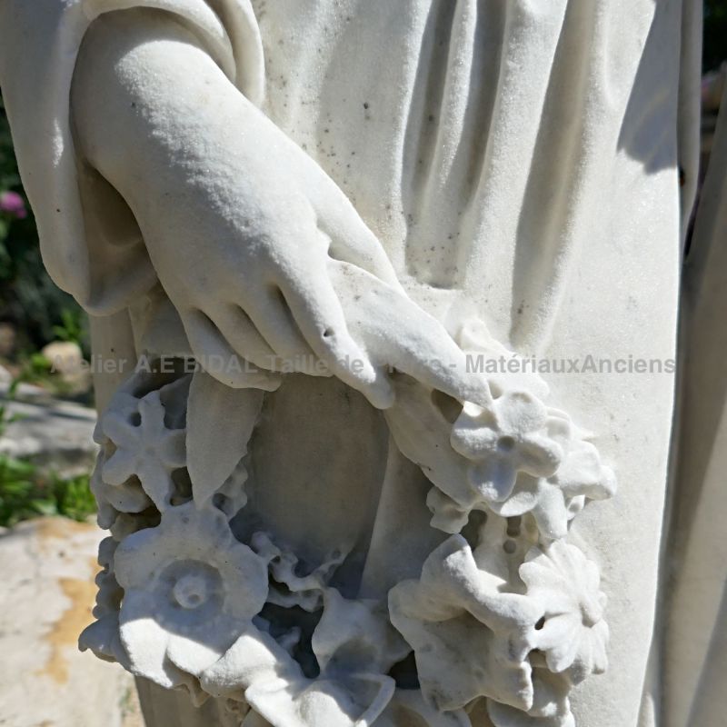 Détail de main tenant une belle couronne de fleurs sur notre sculpture ancienne en marbre blanc | Statue de pleureuse en marbre