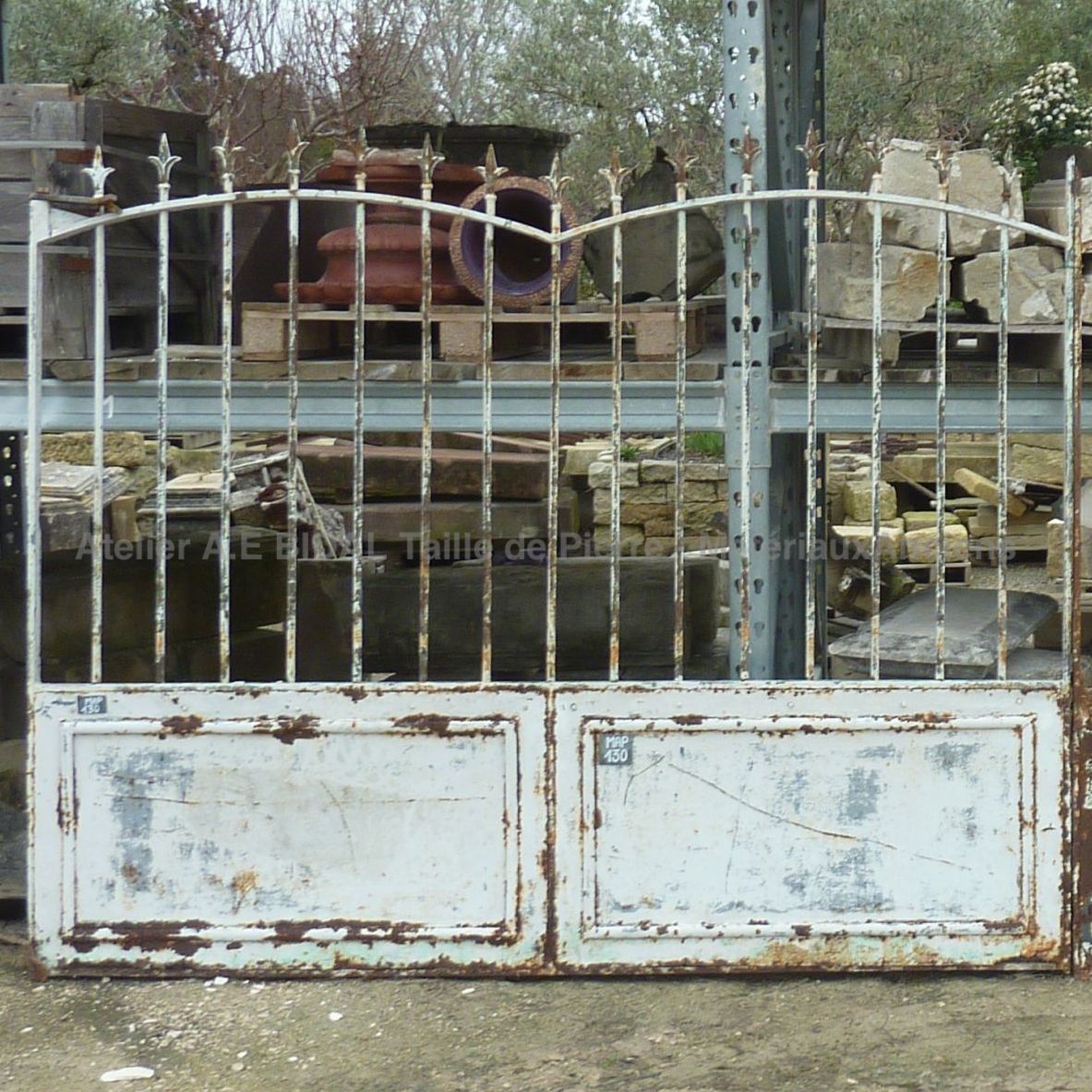Portail ancien en fer forgé blanc patiné par la rouille.