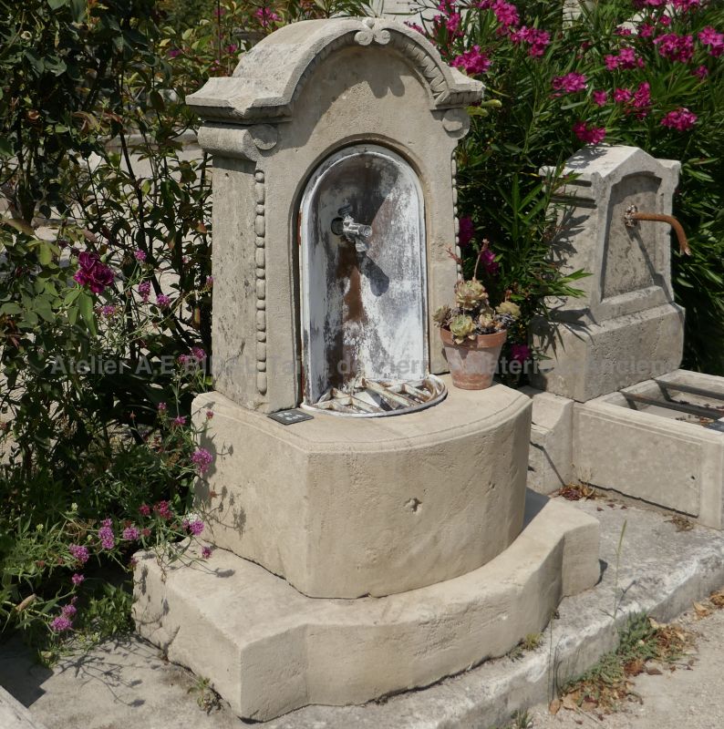 Water pedestal or small wall fountain made of old materials: old stone, wrought iron and metal.